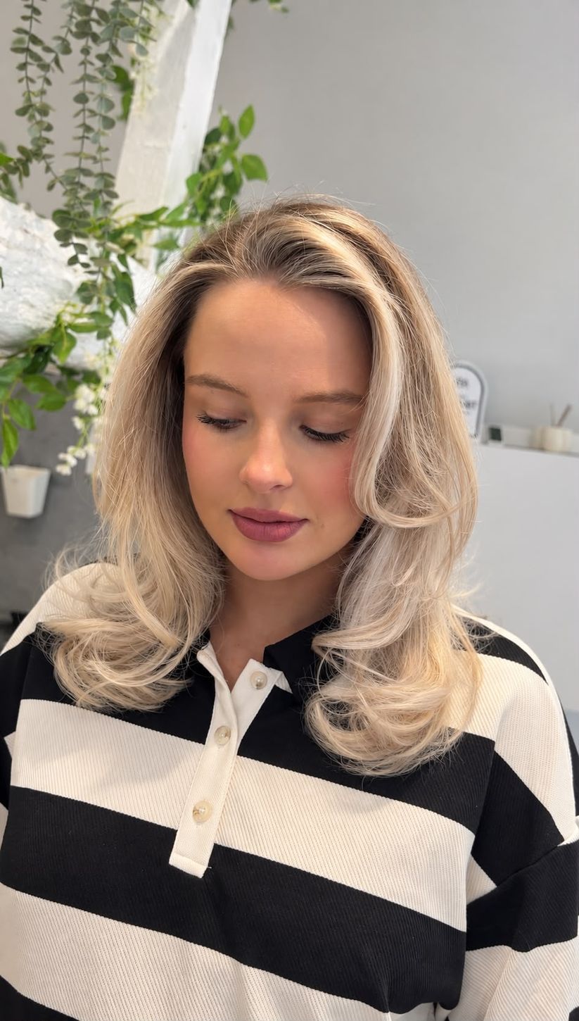 Soft blonde hair with a darker root blend and bouncy, voluminous curled ends