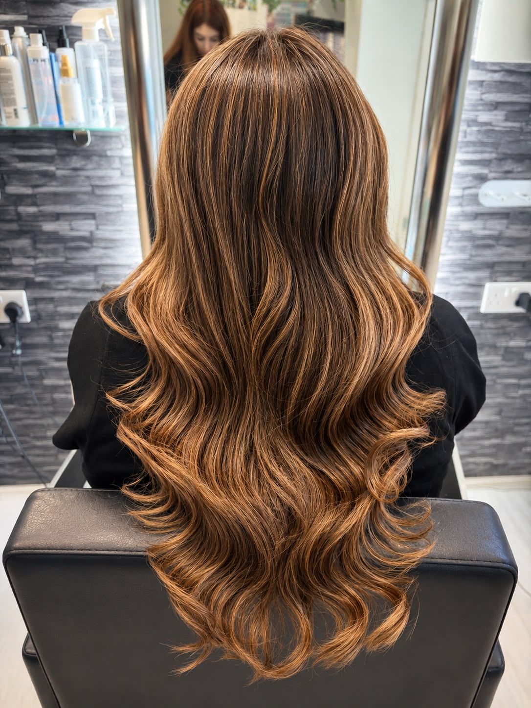 Back view of long brown hair with warm caramel highlights styled in waves